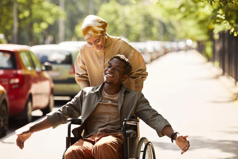 caretaker taking disabled man on wheelchair out on a walk in park