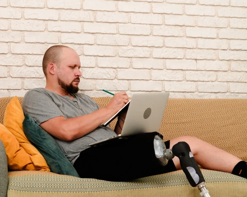 men with prosthetic leg sitting on sofa and working on ipad